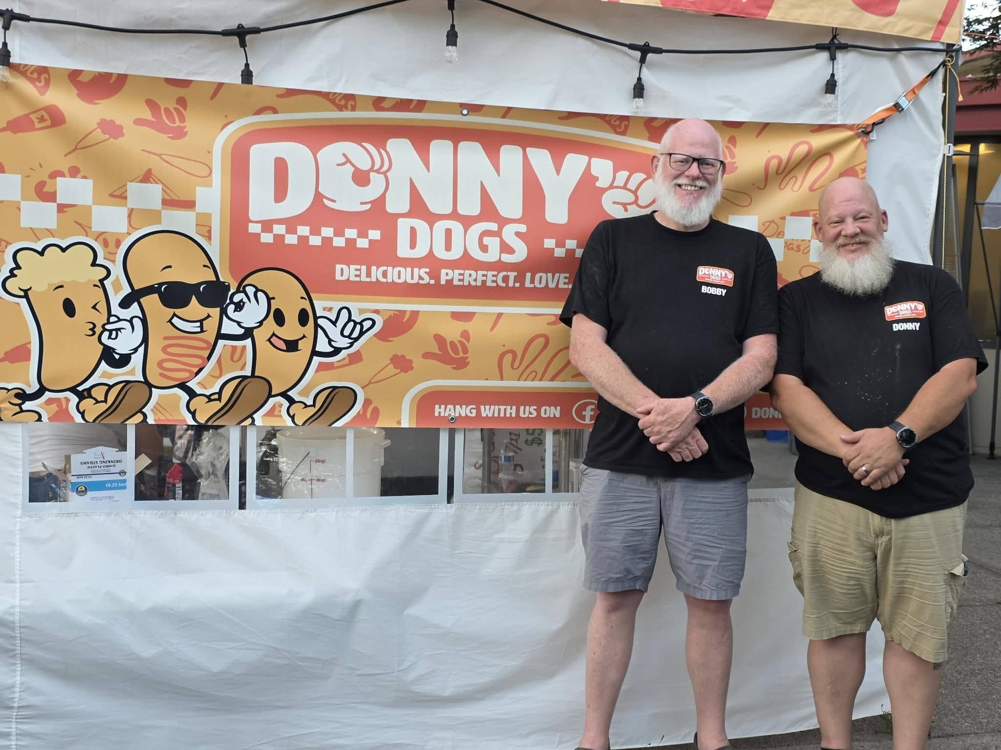 Bobby and Donny of Donny's Dogs standing in front of their food stand banner in Vancouver, WA